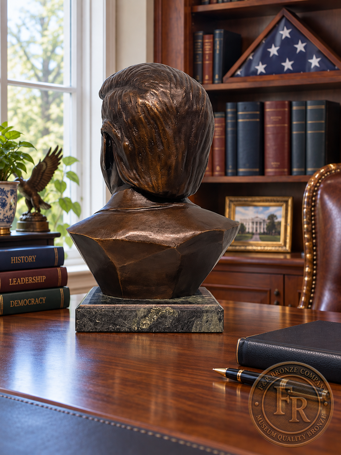 Rear view of a Donald J. Trump presidential bronze portrait on a walnut desk, with books and a folded American flag nearby.
