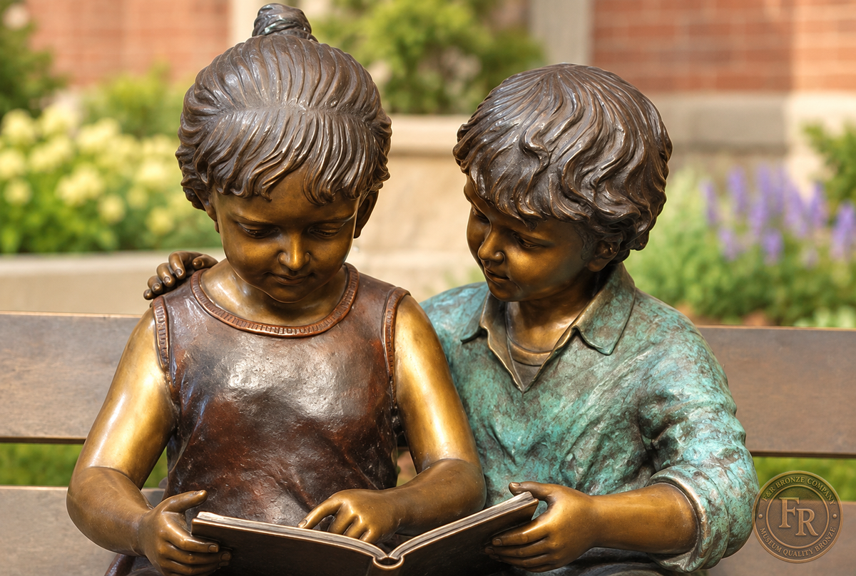Frontal school-garden concept close-up of the bronze boy and girl reading together, with the open book and contrasting patina.