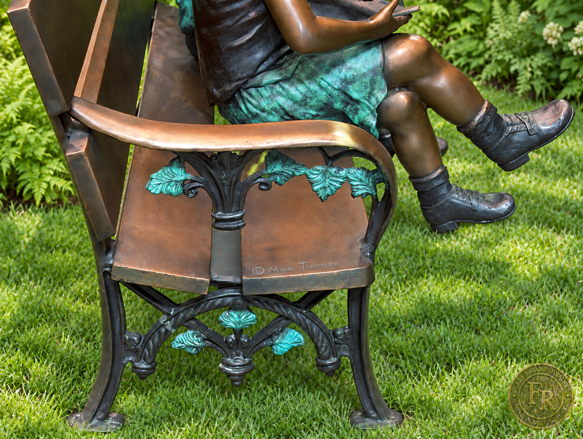 Garden concept side detail of the reading children’s bronze bench, showing its armrest, green leafwork, supports and feet.