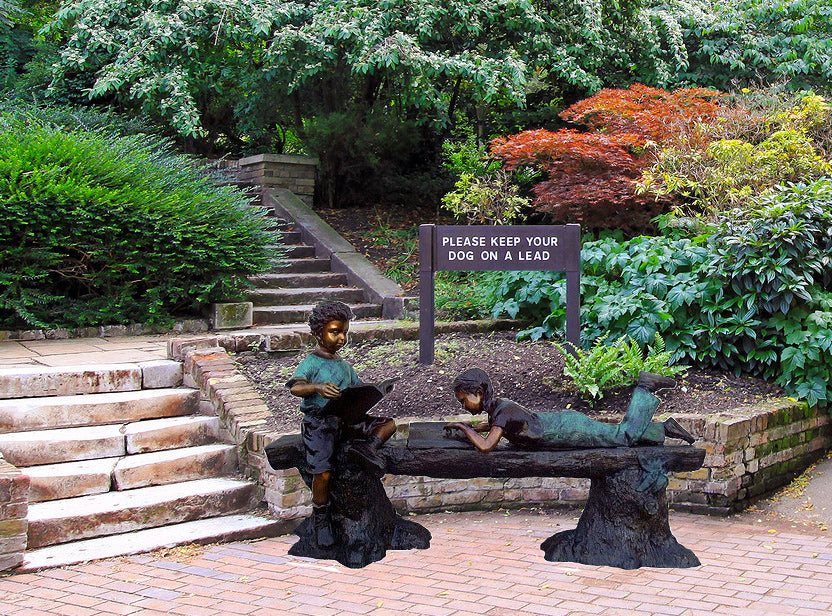 Wide garden view of Reading Time, a bronze sculpture of two children with books on a log beside landscaped steps.