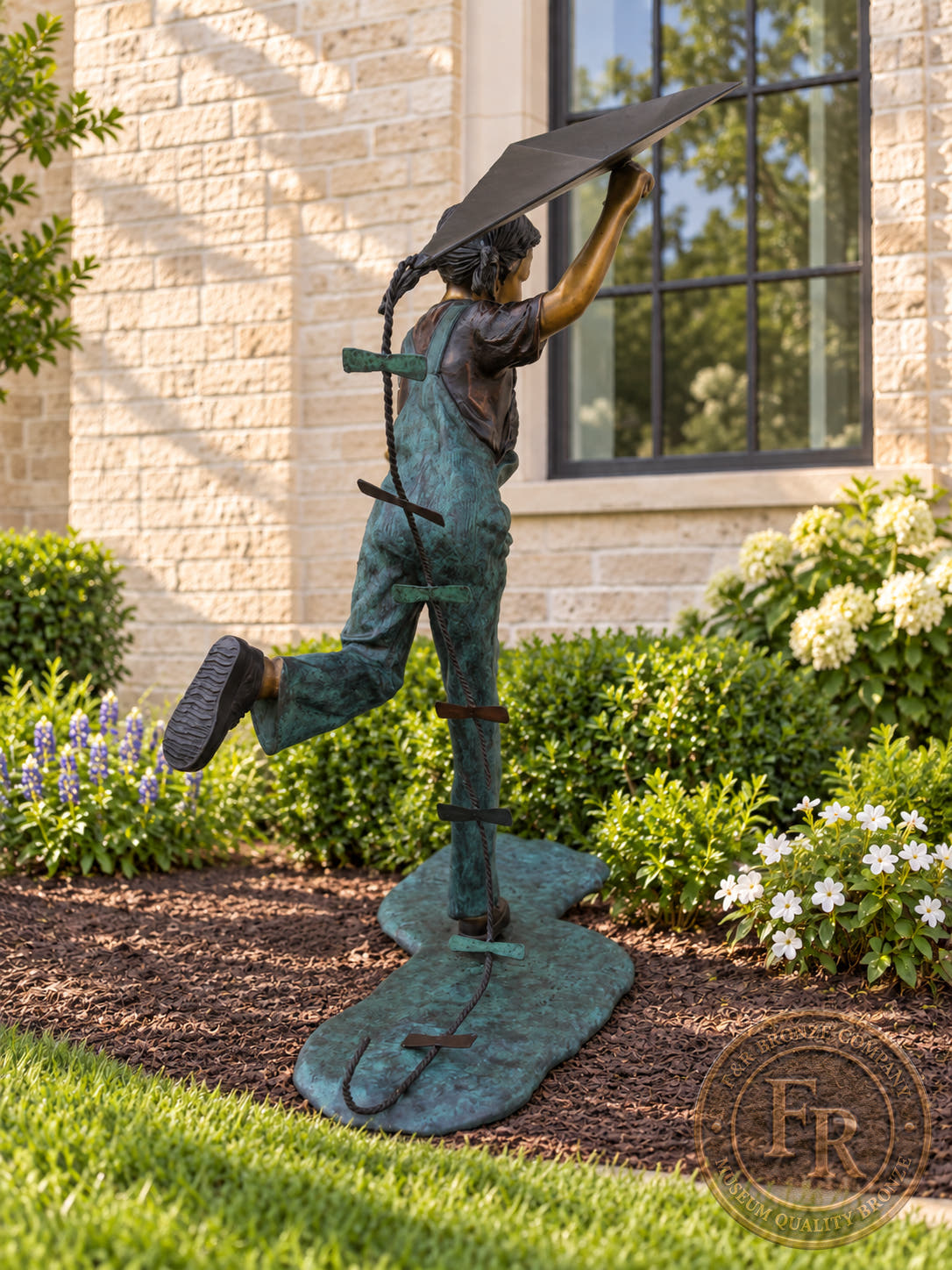 Rear view of the Girl Flying Kite bronze sculpture, showing her braided pigtails, lifted foot, kite tail and sculpted base.