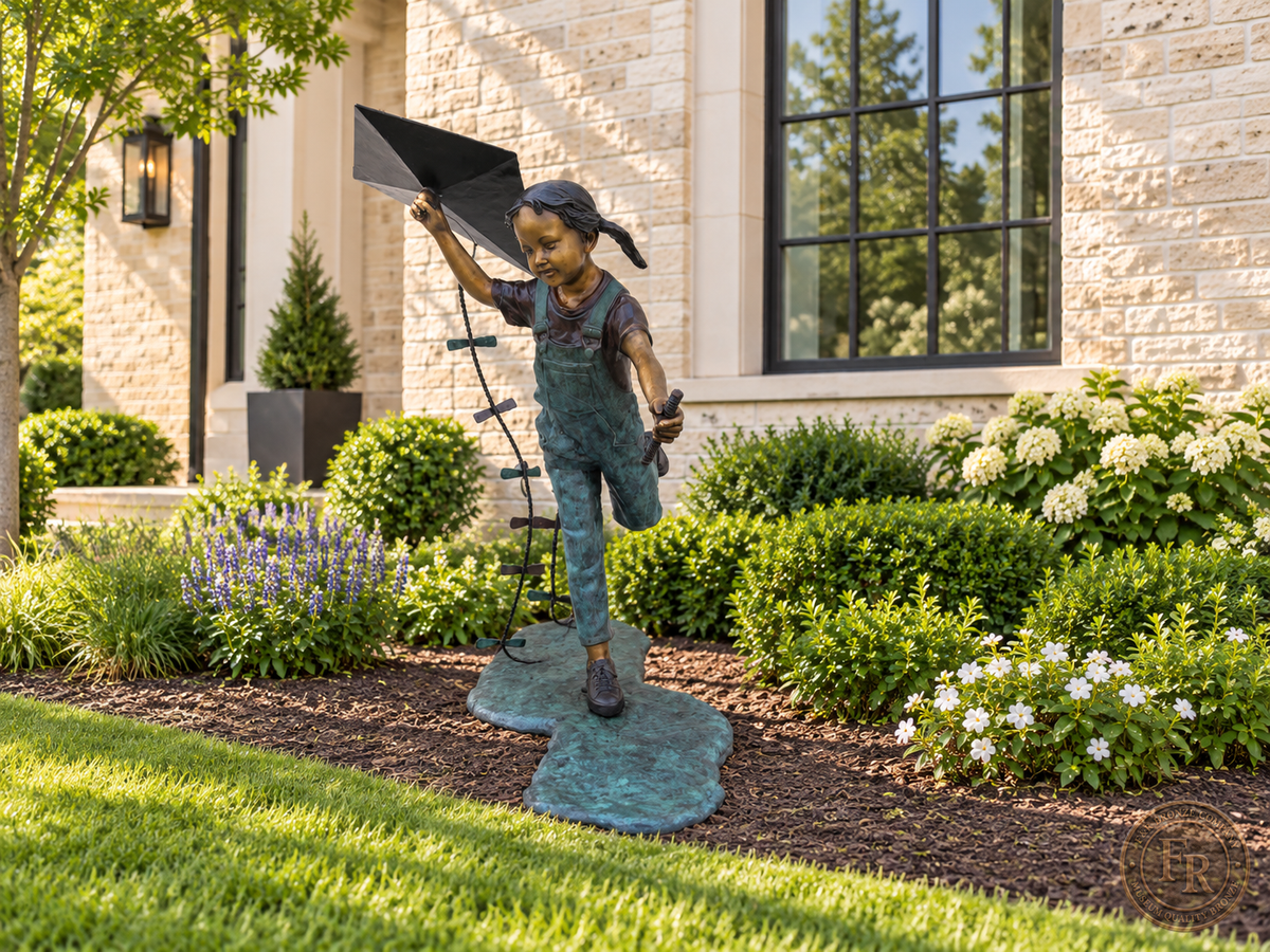 Wide residential garden concept featuring the Girl Flying Kite bronze statue among spring planting beside a brick home.
