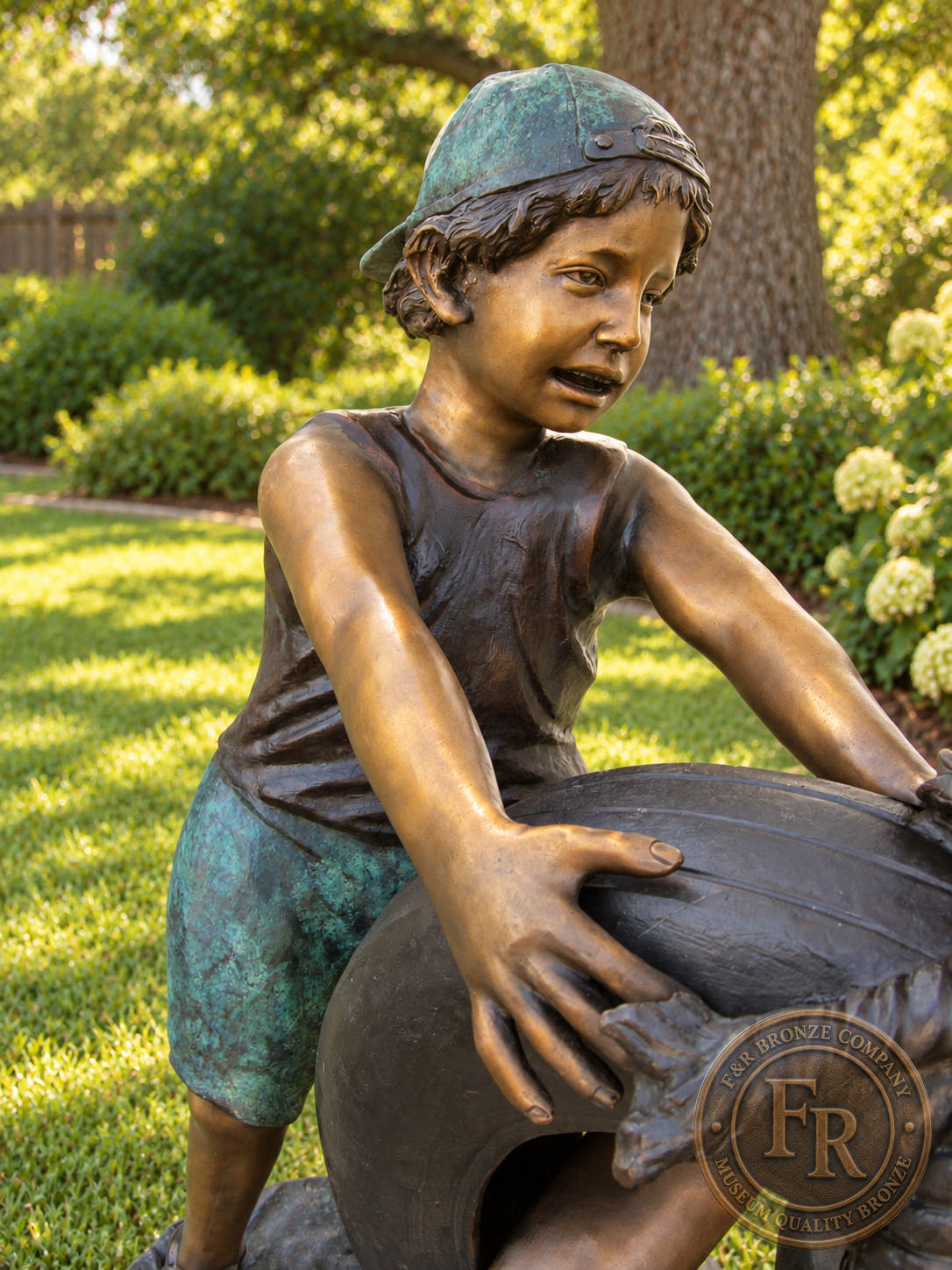 Bronze tire swing statue detail of the smiling boy in a backward cap, with his hands on the tire and turquoise patina on his clothing.