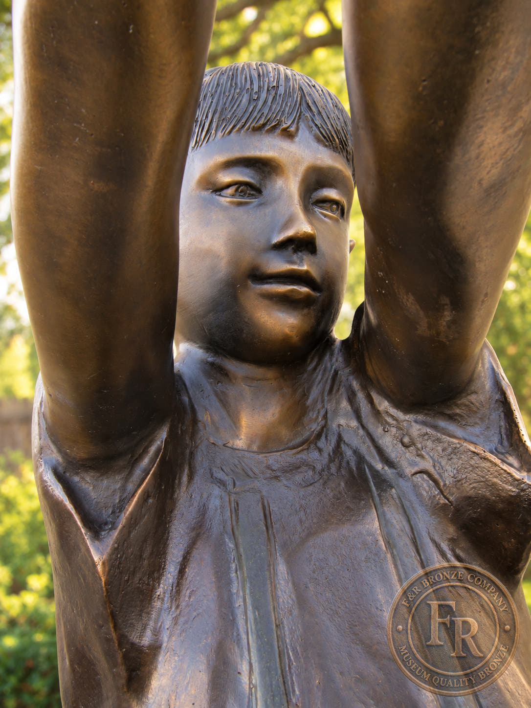 Close-up of the girl’s face and raised arms on the Three Kids Playing with Tire Swing bronze statue by Max Turner.